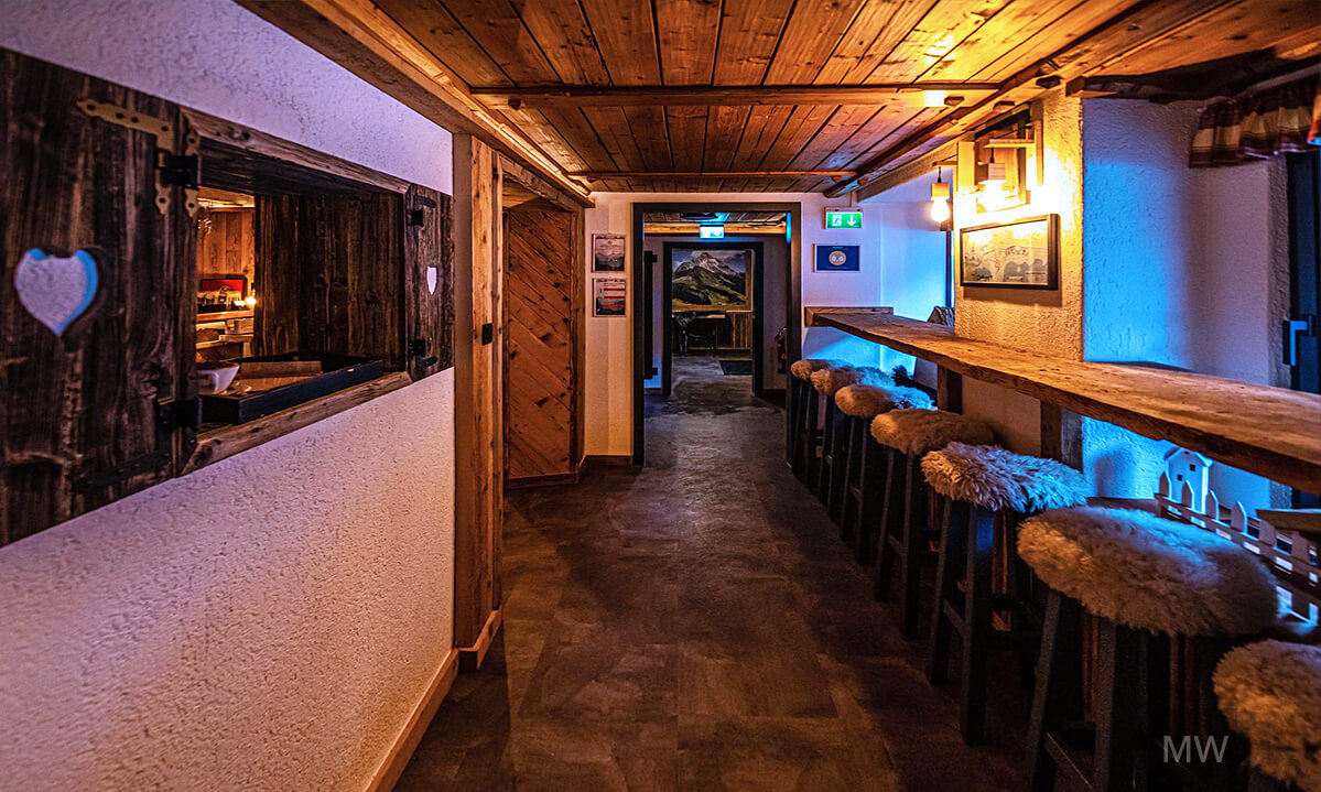 Bar confortabil într-o pensiune rustică cu detalii din lemn și scaune pufoase Bar rustic într-o pensiune, cu tavan din lemn și scaune pufoase.