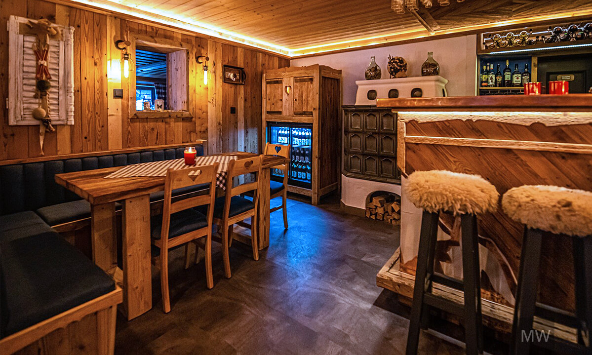 Bar rustic într-o pensiune, cu tavan din lemn și scaune pufoase Bar rustic în pensiunea kitzbuchel alpen pension, cu tavan și pereți din lemn, masă cu față de masă în carouri.