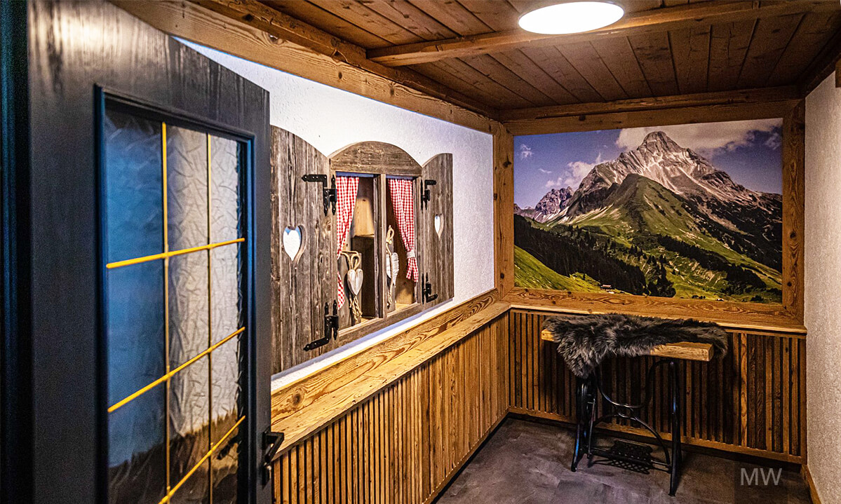 Hol rustic cu decor montan într-o pensiune tradițională Hol rustic cu pereți și tavan din lemn, decorat cu un tablou de peisaj montan și o bancă din lemn cu pătură.