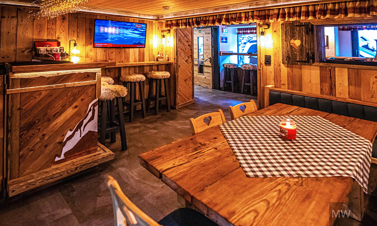 Bar rustic în Kitzbühel Alpen Pension cu tejghea și ecran de munte Bar rustic în Kitzbühel Alpen Pension, cu tejghea din lemn și ecran albastru.