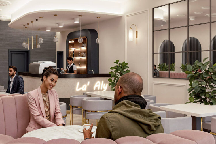 An upscale cafe or lounge area. The interior is adorned with modern design elements, including a curved pink sofa, a sleek counter with a neon sign, and pendant lights hanging from the ceiling. There are two individuals in the foreground: a woman in a pink blazer and a man in a green jacket, engaged in a conversation over a table. In the background, there's a bar counter with a female bartender attending to a customer. The space is well-lit, with large windows allowing natural light to pour in, and is complemented by indoor plants and decorative wall art.
