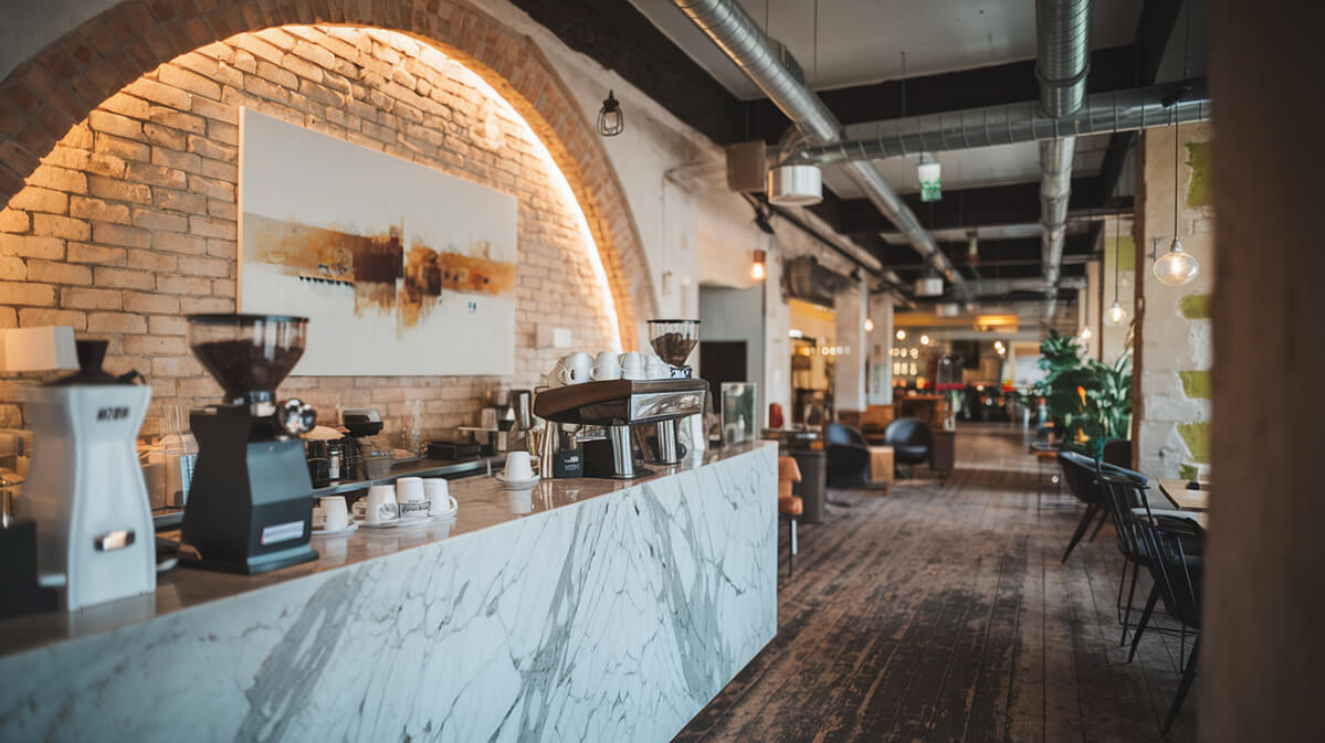 Tejghea de Marmură și Farmec Rustic | Most Wanted Design Cluj Bar moderncu farmec rustic, având un tejghea din marmură, perete din cărămidă semicircular, podea din lemn învechit și instalații expuse.