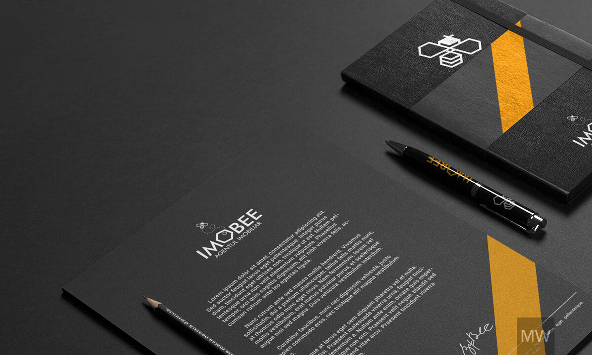 IMOBEE Branding Setup A branding setup for IMOBEE, featuring a black notepad with the logo and a pencil, alongside a black-and-yellow notebook with the same branding and a matching pen.
