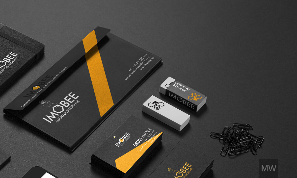 IMOBEE Branding and Stationery Collection A branding and stationery setup for IMOBEE, featuring a black notebook, a black envelope with an orange diagonal stripe, two branded white USB sticks, and a stack of black business cards with the IMOBEE logo.