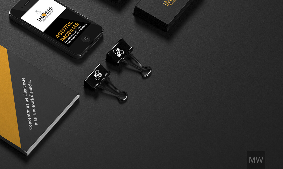 Dark-Themed Branding Setup A dark-themed branding setup for 'IMOBIL,' including a notepad, smartphone, banners, business cards, and binder clips with house and bee icons.