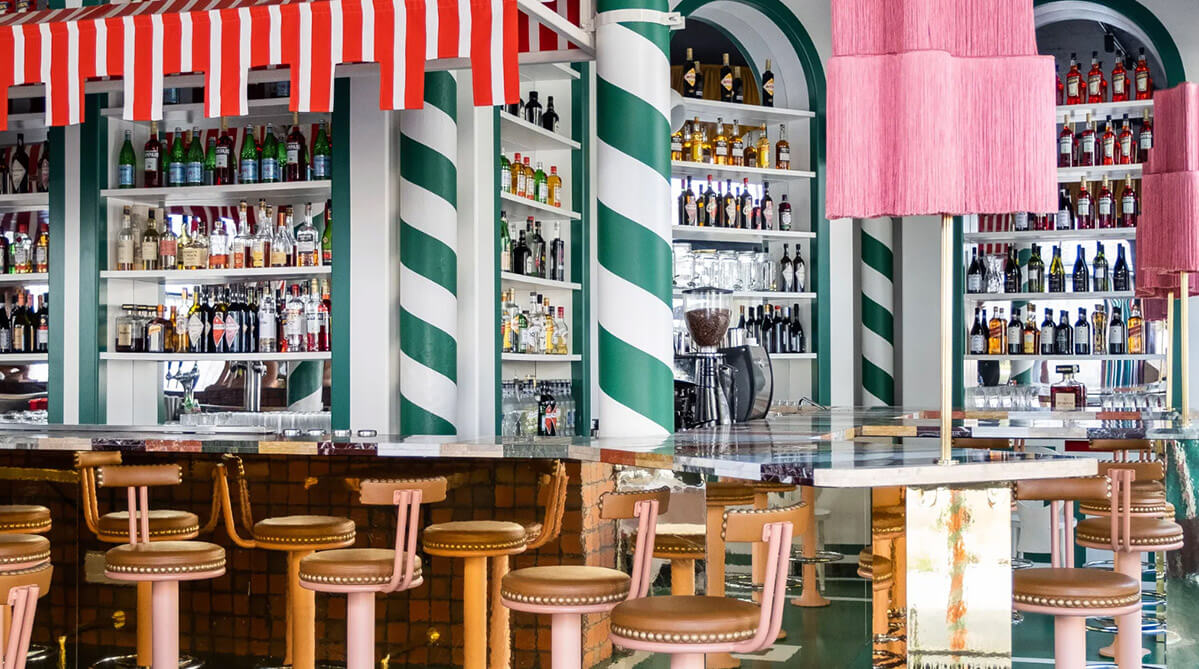 Eclectic Bar with Colorful Decor Vibrant cafe interior with green and white striped walls, a red and white awning above the bar, and pinkish-brown studded bar stools.