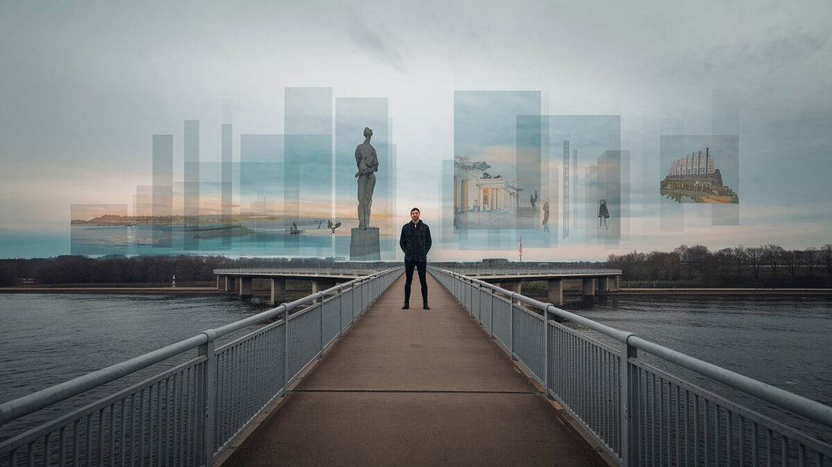 Man at the Edge of a Bridge with Floating Memories A man stands at the edge of a bridge, facing a path ahead, with translucent images of people, a landscape, a statue, and a building hovering above the water.