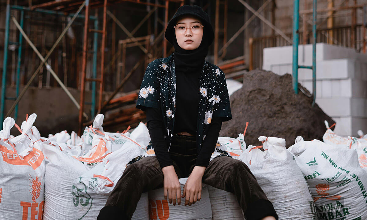 Portret urban pe un șantier – contrast între stil personal și spațiu industrial Tânără stând între saci albi pe un șantier cu schelă metalică în fundal, purtând o jachetă florală și adidași albi.