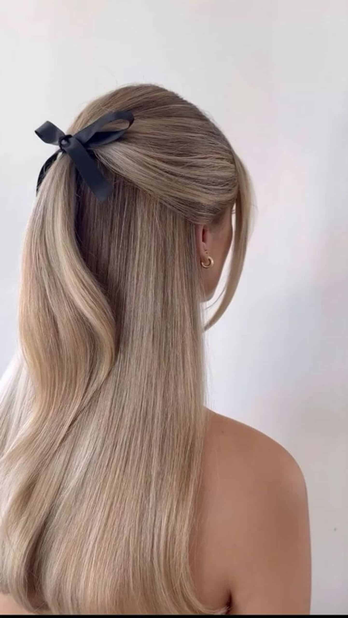 Elegant Ponytail with Black Ribbon and Gold Hoop Earring Person with long straight blonde hair tied back in a black ribbon bow, wearing a gold hoop earring against a plain white background.