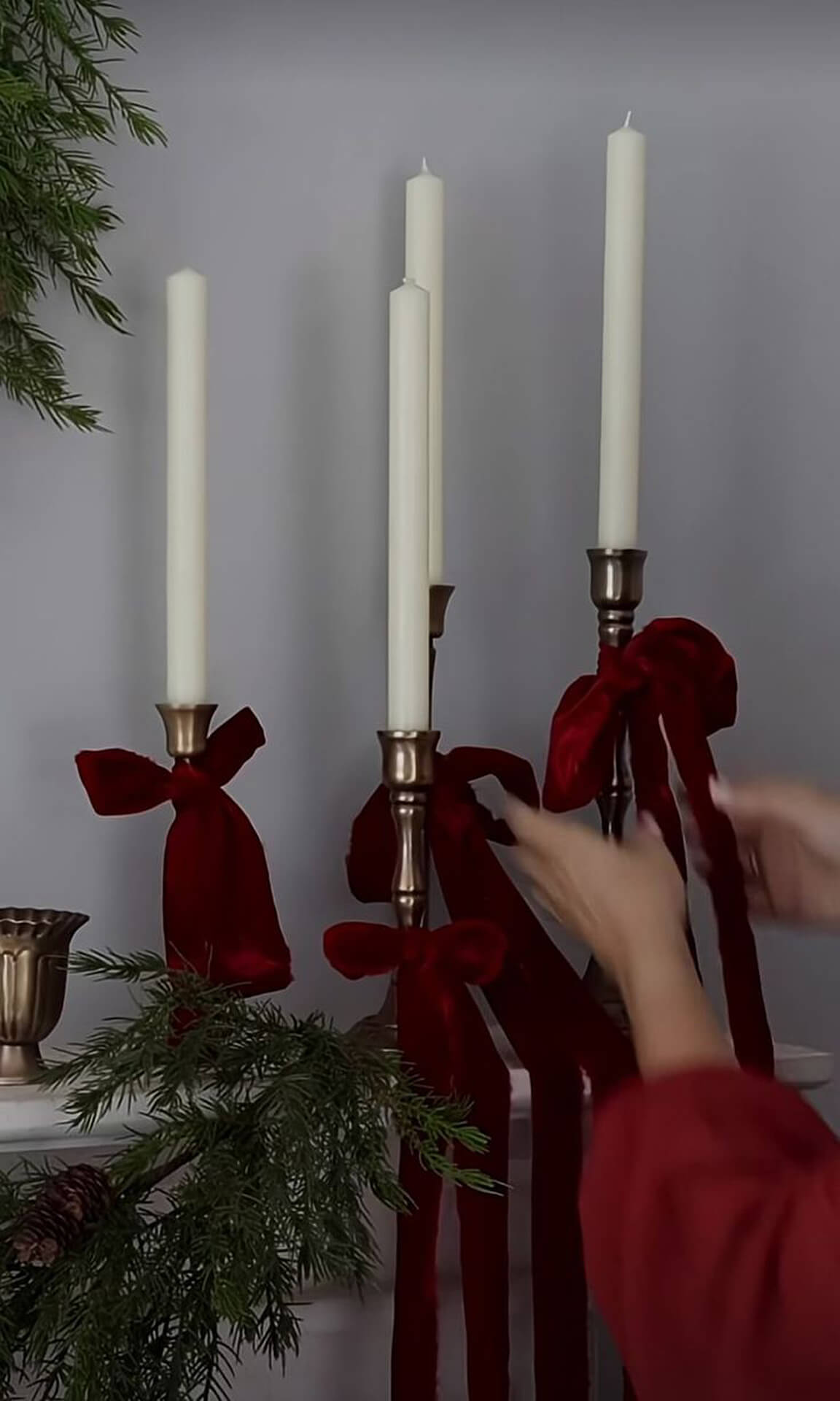 Elegant Christmas Candles with Red Ribbons and Natural Greenery White candles with red ribbon bows, pine branches, and gold candle holders