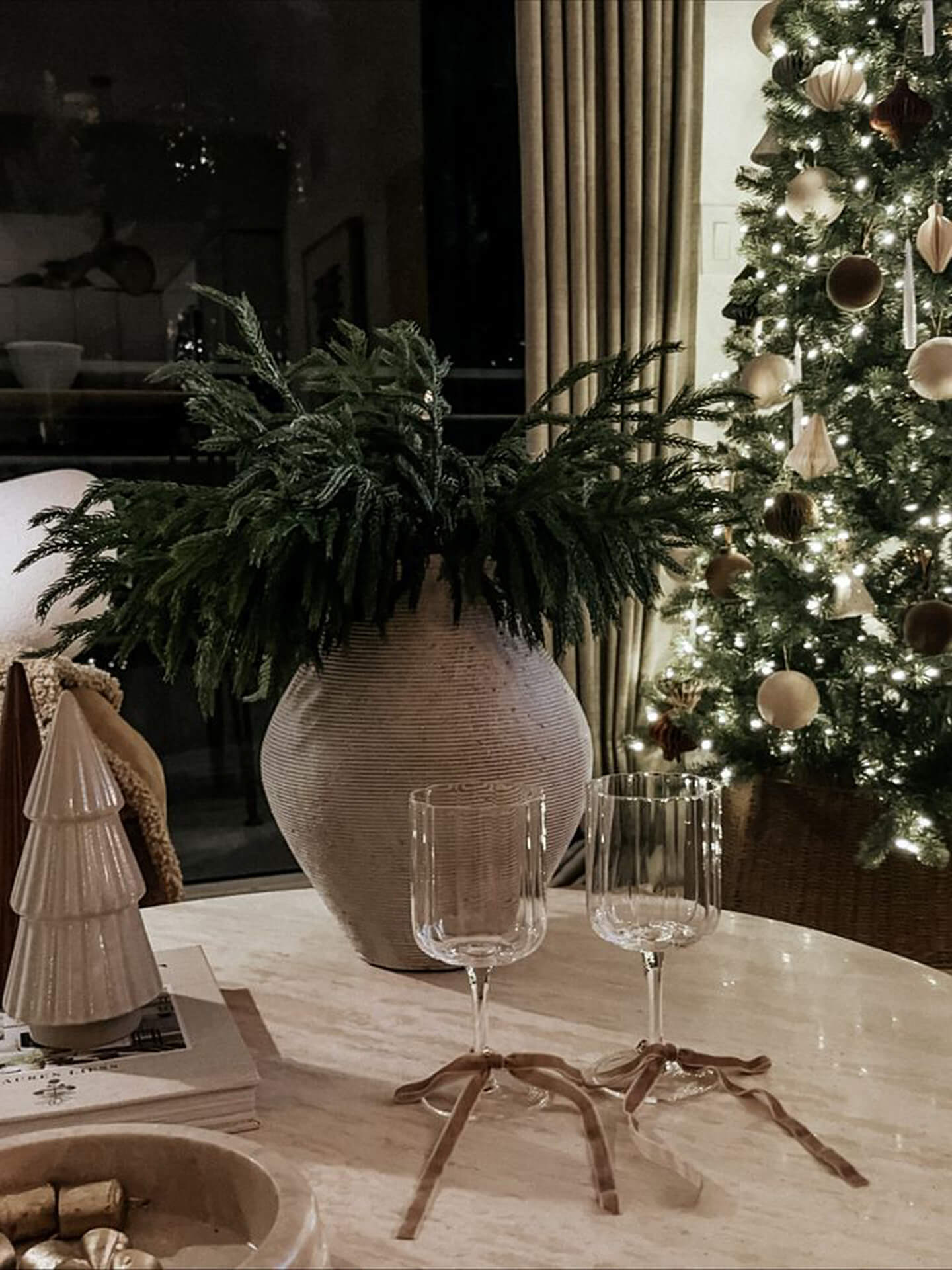 Festive Christmas Table Decor with Tree and Wine Glasses Cozy Christmas setting with decorated tree, wine glasses with ribbons, and potted plant on table