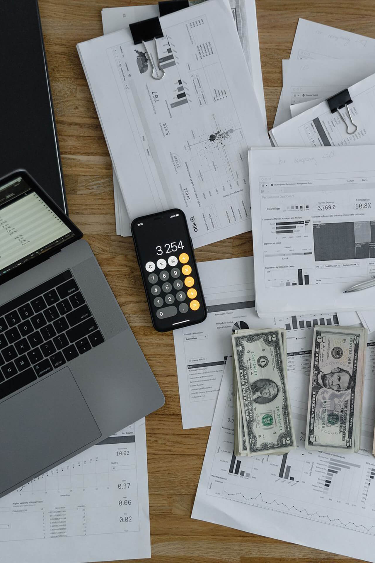 Financial Planning Workspace with Charts and Calculator Cluttered desk with financial charts, laptop, calculator showing 3254, and cash